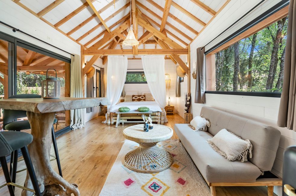 Intérieur du lodge Goa de Calviac avec le lit, le canapé, une table de salon, et une table haute en bois