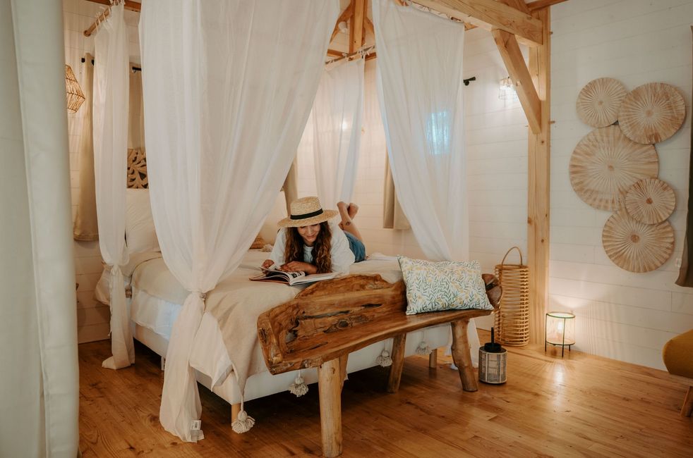 A woman wearing a hat reads a book on the bed of the Shiva lodge in Calviac