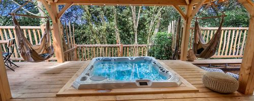 Terrasse du lodge Jaya de Calviac Terrasse du lodge Jaya avec spa et deux hamacs avec vu sur les bois
