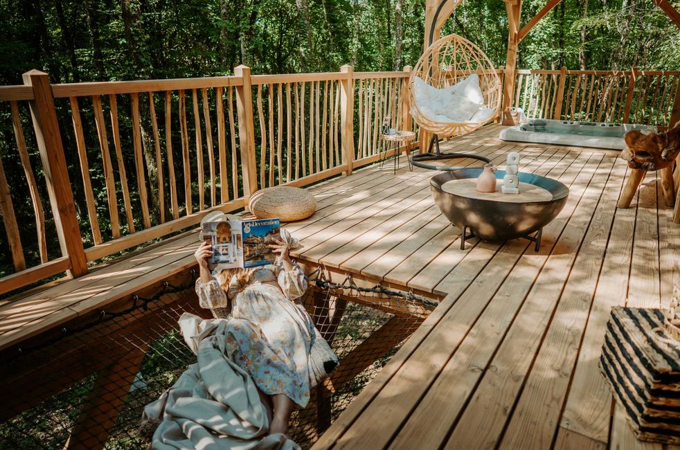 Terrasse du lodge Kali avec une femme allongée sur le filet lisant un livre, une table, un siège et une vue sur les bois